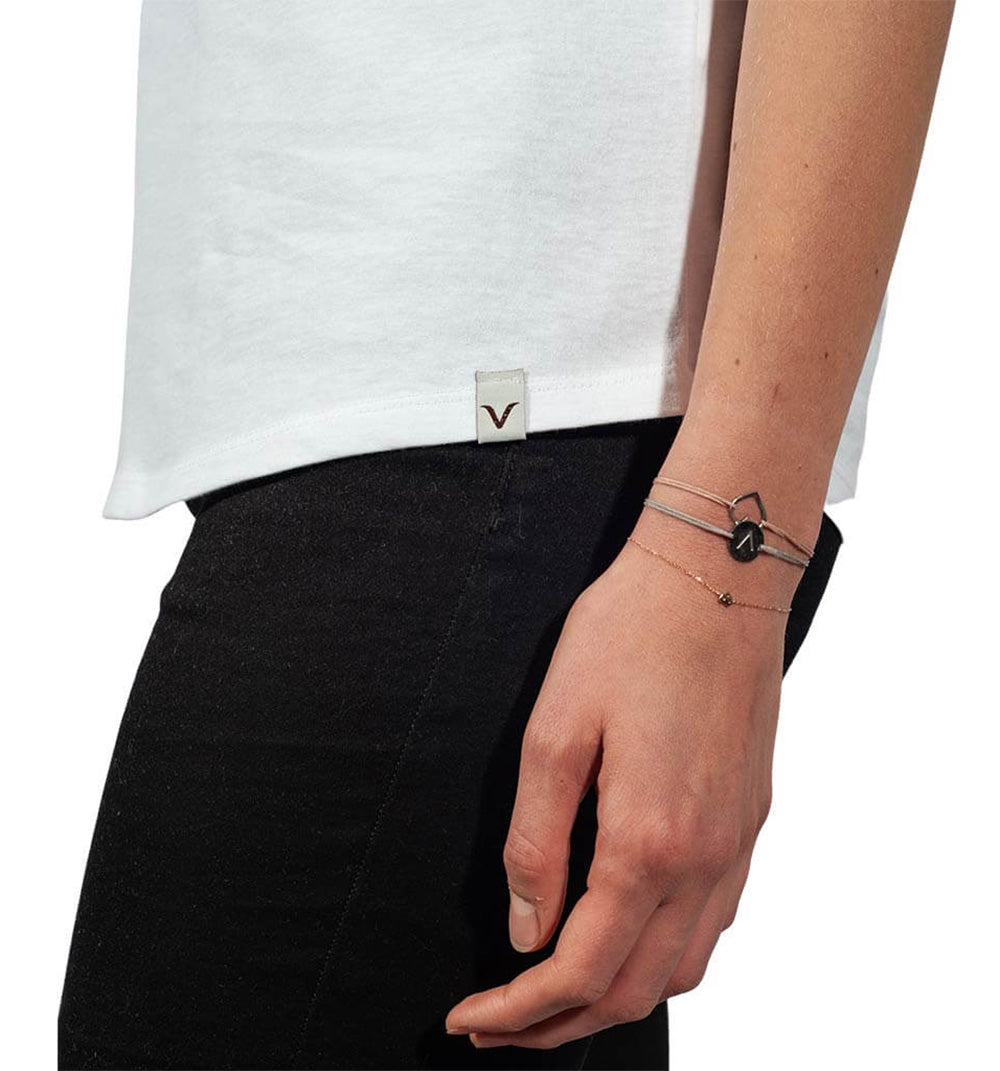 Jemand trägt ein weißes „T-Shirt Bowlmates“ von Verival Bio und eine schwarze Hose, mit einem Armband am Handgelenk.