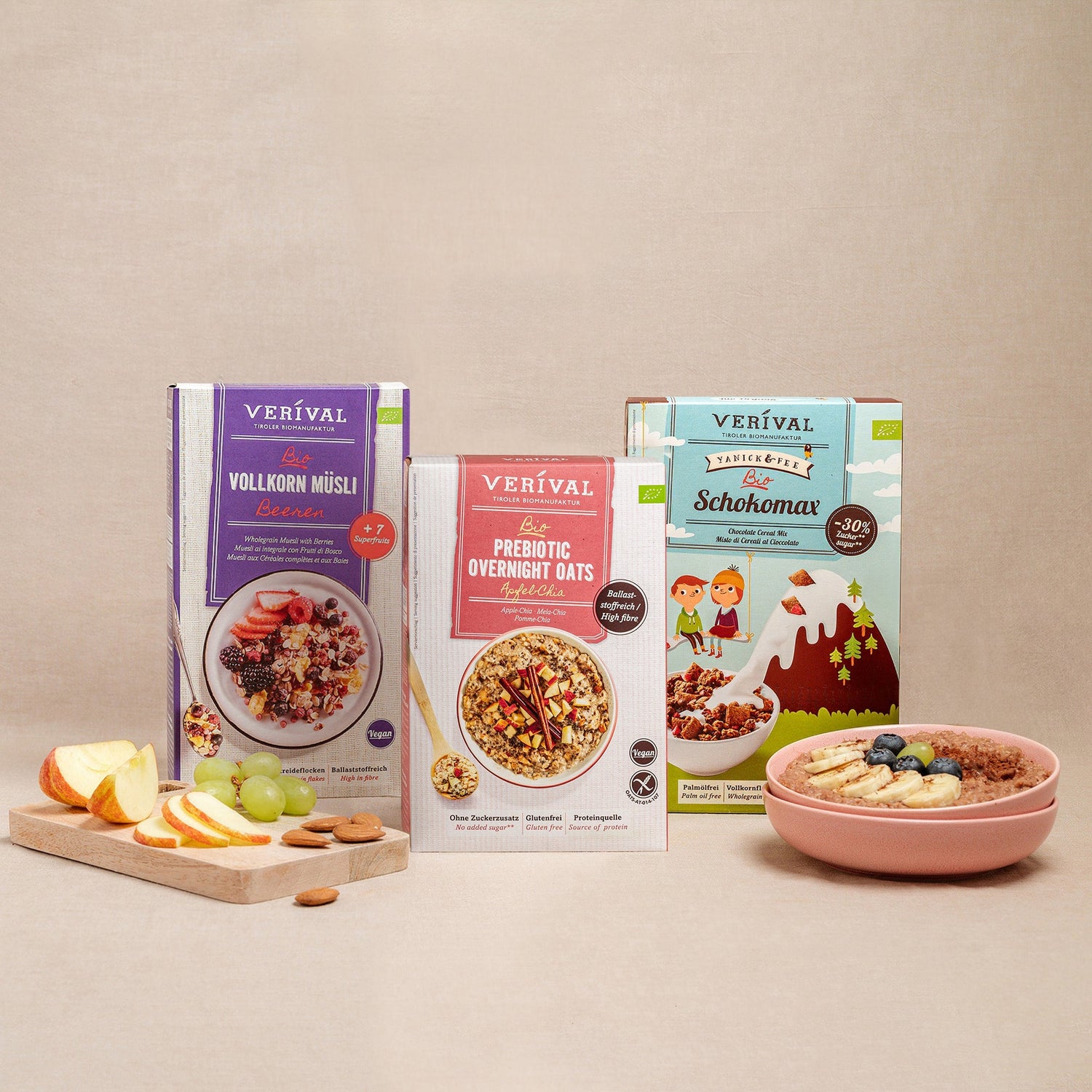 Three Verival cereal boxes are on display, including Whole Grain Muesli, Prebiotic Overnight Oats, and Schokomax. In front of them are a bowl of muesli and sliced fruit on a cutting board.