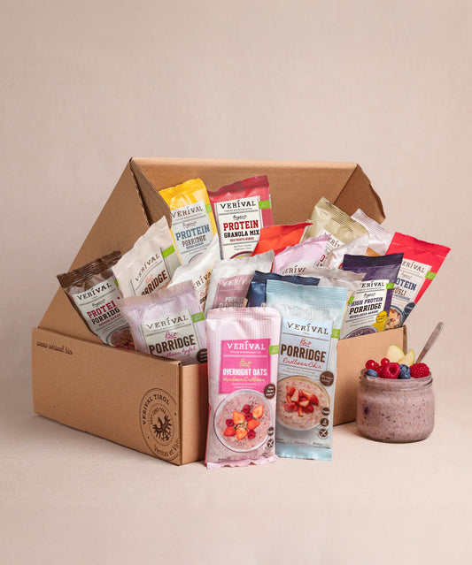 Die Verival Bio GmbH 30 Tage Gesund frühstücken Box mit verschiedenen Frühstücks-Sachets steht neben einer Schüssel mit Beeren und Overnight Oats - perfekt für gesunde Frühstücksideen mit veganen Bio Zutaten.