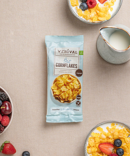 Auf einem Tisch steht eine Einzelportionspackung ungesüßte Cornflakes knusprige Frühstücksoption, daneben Schüsseln mit diesen knusprigen Leckereien, Milch und frischen Beeren.