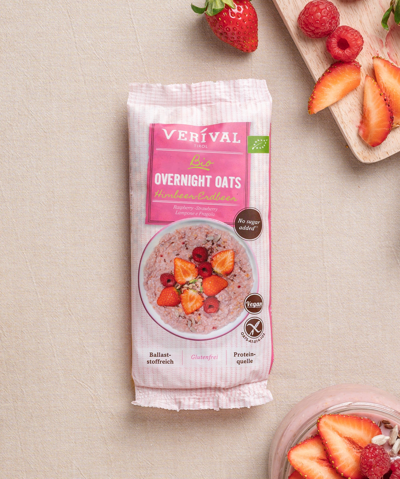 Eine Packung Erdbeer-Chia Porridge der Verival Bio GmbH steht auf einer hellen Unterlage, umgeben von frischen Erdbeeren und einem Glas pflanzlichem Porridge mit Früchten – ideal für dein Frühstück.