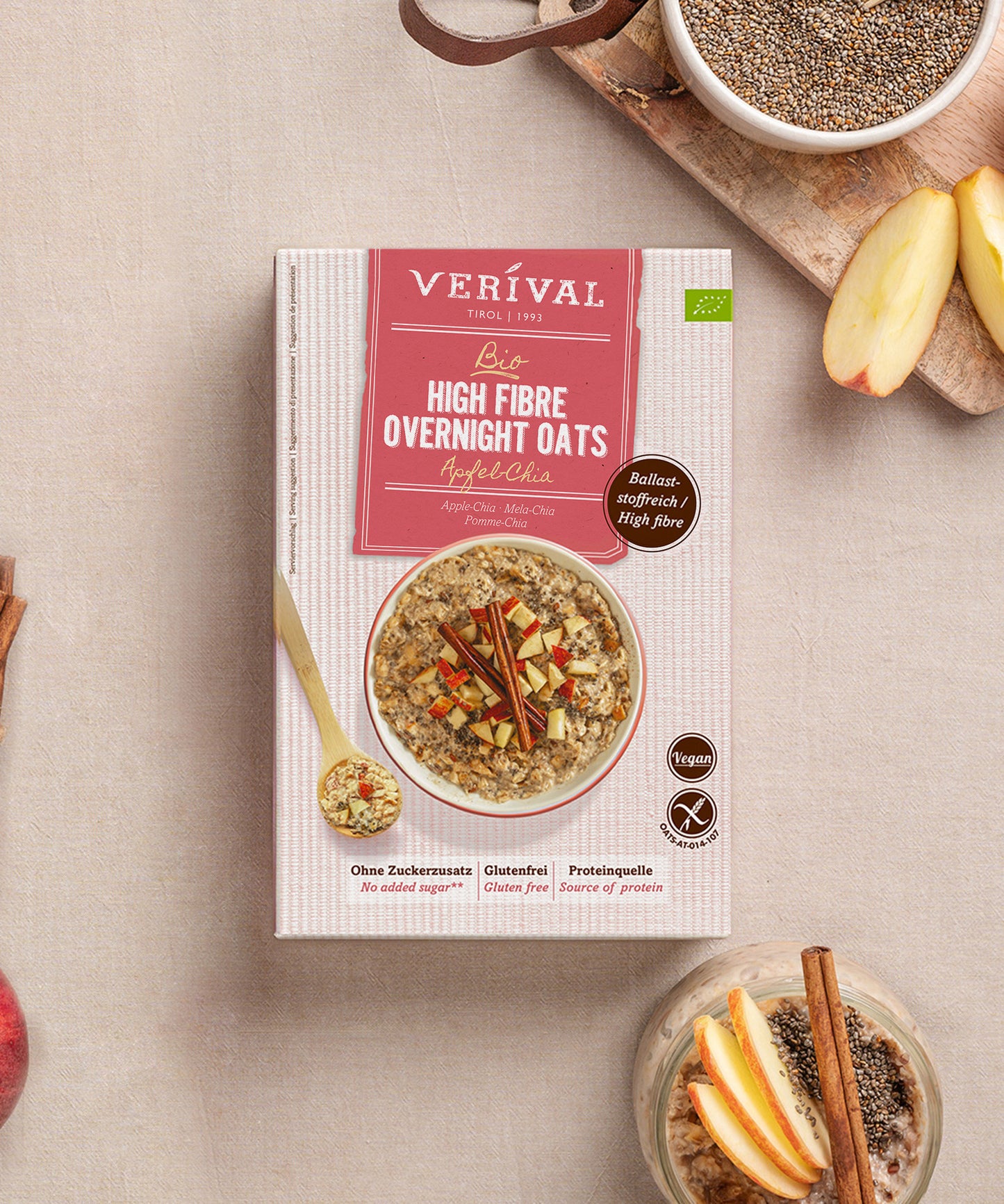 Eine Packung Verival Bio GmbH Bio High Fibre Oats Apfel-Chia steht auf einer hellen Fläche, umgeben von einer Schale mit veganen Haferflocken, Apfelscheiben, Zimtstangen und Chiasamen - reich an Ballaststoffen.