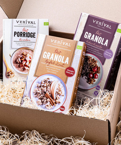 Das Set "All I Want For Breakfast" der Verival Bio GmbH enthält drei Sorten - Porridge, Apfel-Zimt-Granola und Haselnuss-Kakao-Granola - als Frühstücks-Geschenkset in einer Pappschachtel mit Strohverpackung.